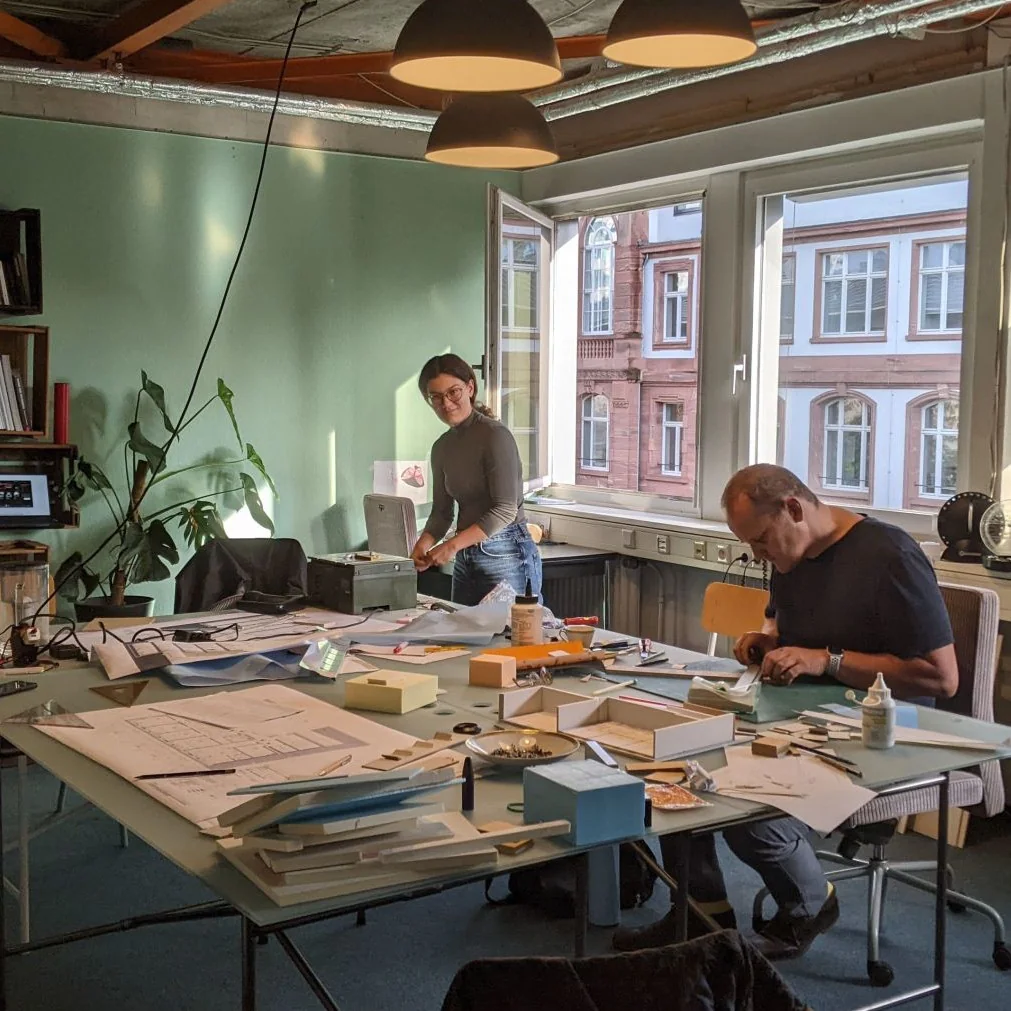 An einem Tisch wird am Modell des Neubaus gearbeitet